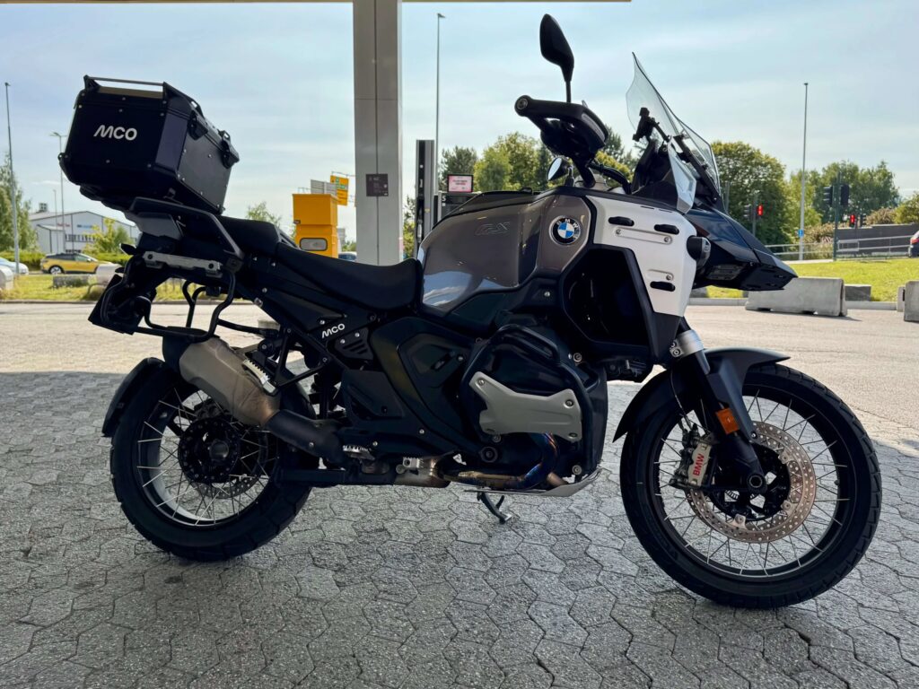 BMW R 1300 GS Adventure med stor tank, eikerhjul og MCO-bagasje, parkert ved en bensinstasjon