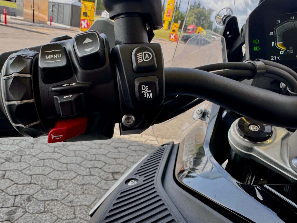 Venstre håndtak på BMW R 1300 GS Adventure med knapper for meny, lys, automatisk/manuell girmodus og horn. Instrumentdisplayet viser girindikator og 21 °C