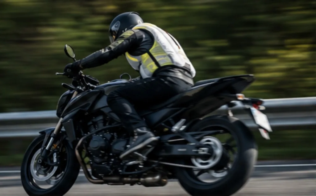 Motorsyklist i fart på landevei med hjelm, skinndress og hvit airbagvest med gule reflekser