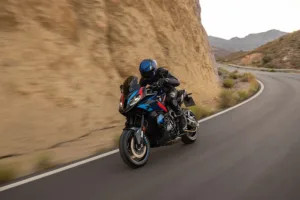 BMW M 1000 XR i blått, rødt og svart M-design i sving på fjellvei med bratt bergvegg på innsiden. Beepi.no / Bikelifenorge.no