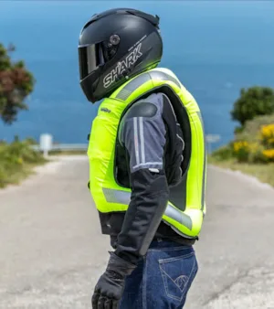 Motorsyklist sett fra siden med påblast gul airbagvest, hjelm og beskyttelsesutstyr, med havet i bakgrunnen