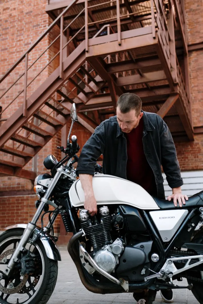 Mann som inspiserer motor på en Honda CB1100 motorsykkel foran en murbygning med branntrappe
