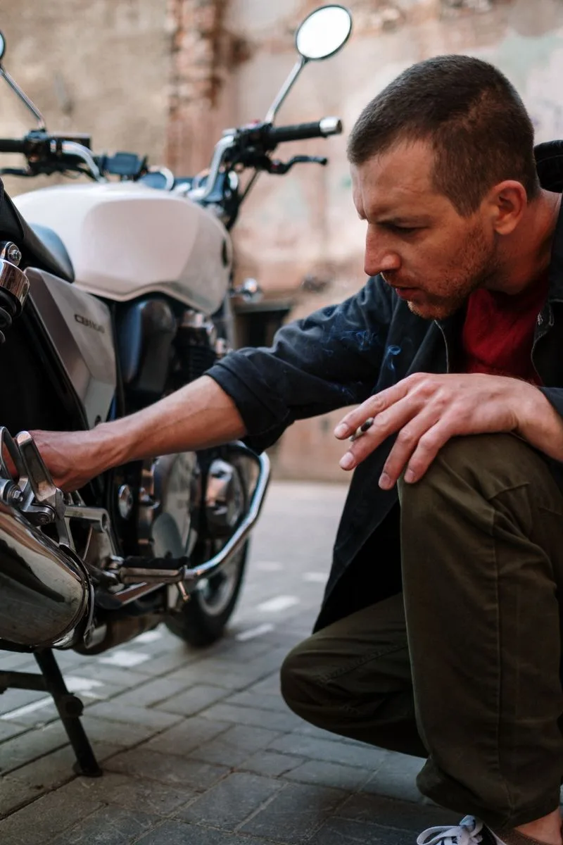 A man focusing on fixing a motorcycle outdoors on a sunny day.